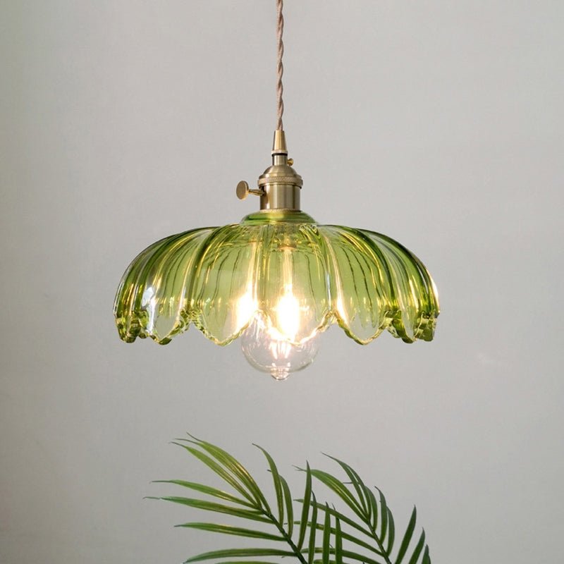  Een stijlvolle hanglamp met een amberkleurige glazen kap met golvende randen, die een warme gloed verspreidt. De lamp is bevestigd aan een gouden fitting met een gedraaide kabel, waardoor een vintage uitstraling ontstaat. De lichtbron is zichtbaar en geeft een uitnodigende sfeer aan de ruimte, terwijl de subtiele achtergrond de elegantie van de lamp benadrukt.